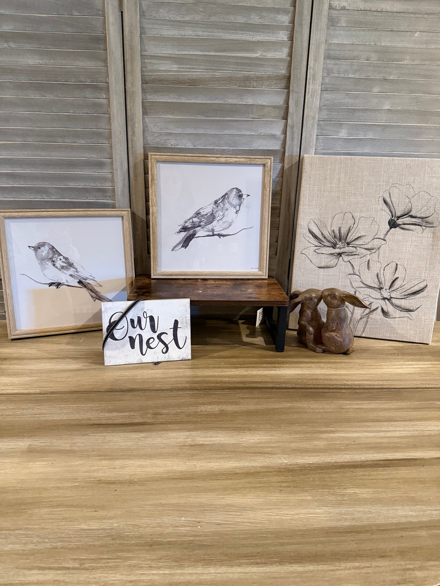 Nature-inspired home décor featuring neutral bird sketches in wood frames, a floral canvas with soft linen texture, 'Our Nest' farmhouse sign, rustic wooden display riser, and a pair of brown bunny figurines. A perfect setup for spring, cottagecore, or farmhouse-style decorating."