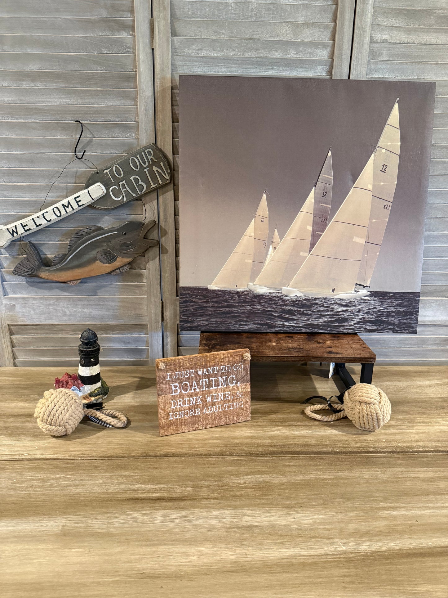 Nautical cabin décor with sailboat art, fish sign, lighthouse figurine, rope accents, and a fun boating quote—perfect for lake or coastal home styling.