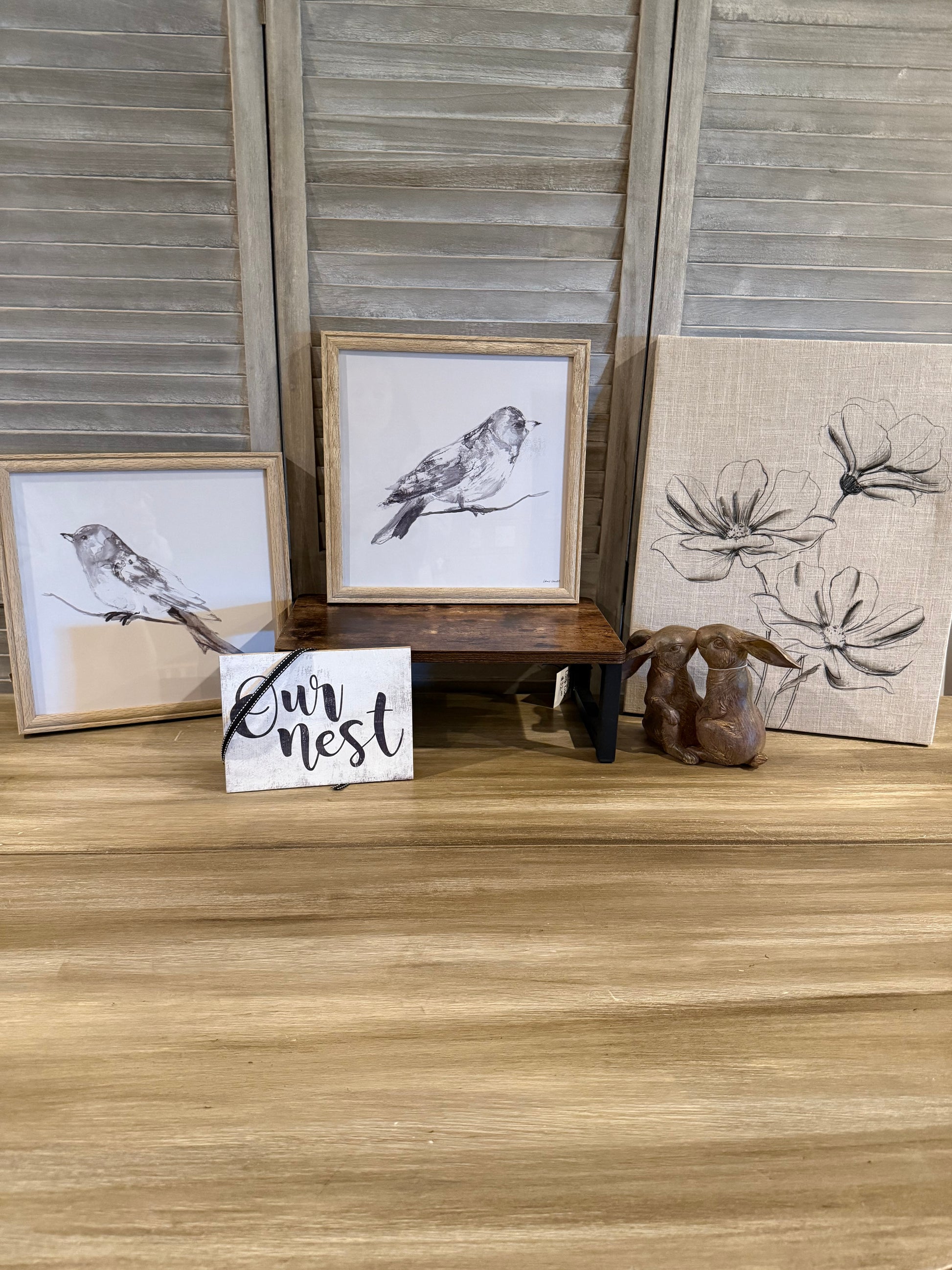 Nature-inspired home décor featuring neutral bird sketches in wood frames, a floral canvas with soft linen texture, 'Our Nest' farmhouse sign, rustic wooden display riser, and a pair of brown bunny figurines. A perfect setup for spring, cottagecore, or farmhouse-style decorating."