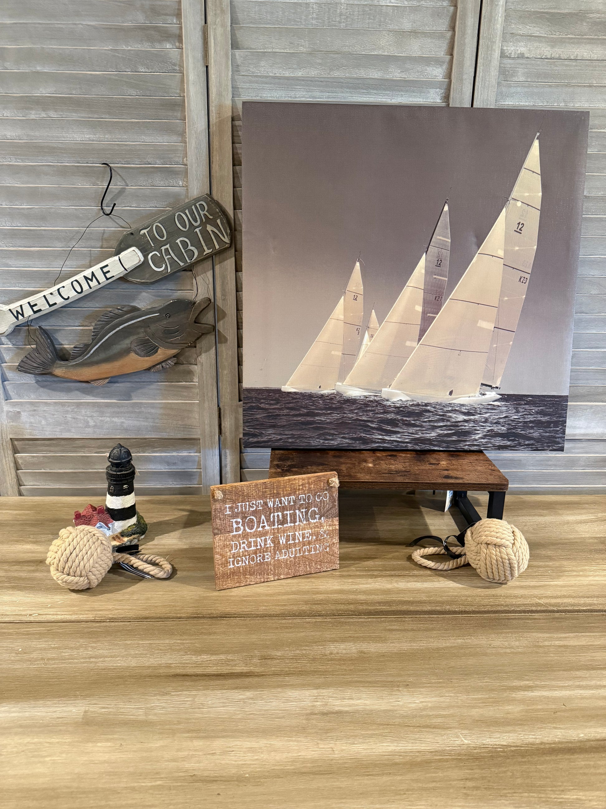 Nautical cabin décor with sailboat art, fish sign, lighthouse figurine, rope accents, and a fun boating quote—perfect for lake or coastal home styling.